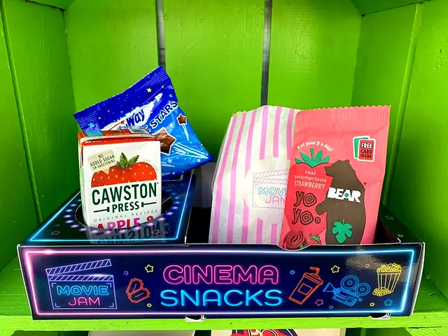 Neon Cinema Snacks tray with crisps, juice and sweets against a green wall