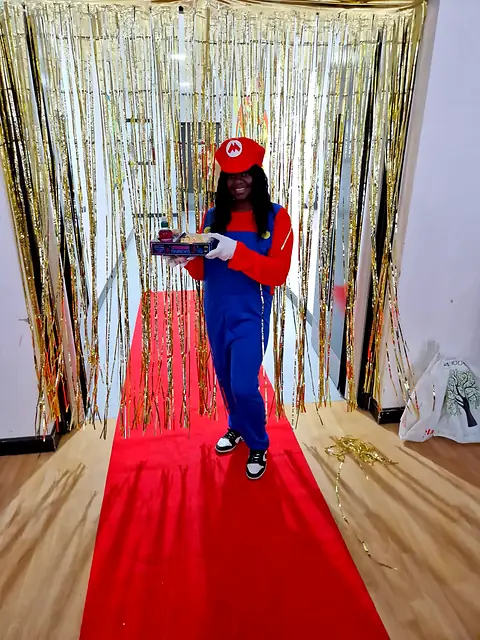 Person in a plumber costume carrying a snack tray down a red carpet