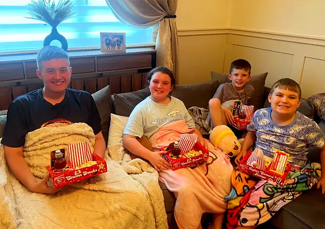 Family relaxing on a sofa under blankets with red snack trays