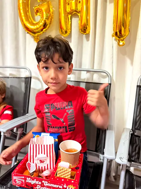 Boy giving a thumbs up behind a red snack tray of popcorn