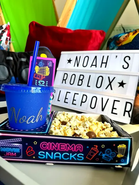 Personalised blue cup and neon snack tray beside a Roblox sleepover sign