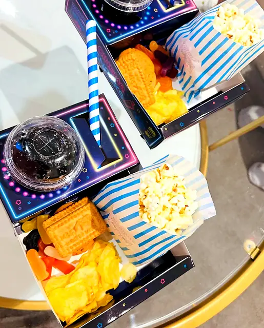 Overhead view of neon trays with popcorn, sweets and drinks