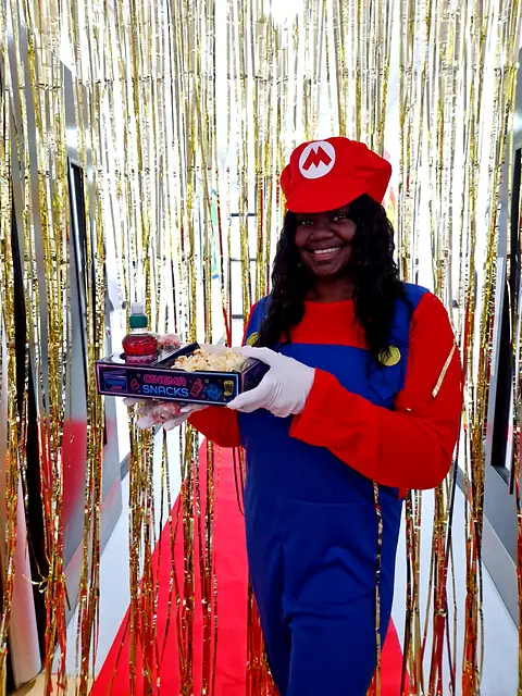 Person in a plumber costume holding a snack tray on a red carpet