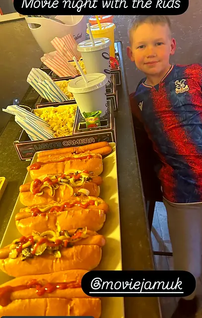 Boy beside a long line of trays filled with hot dogs and popcorn