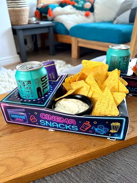Neon Cinema Snacks tray with a can, nachos and dip on a table