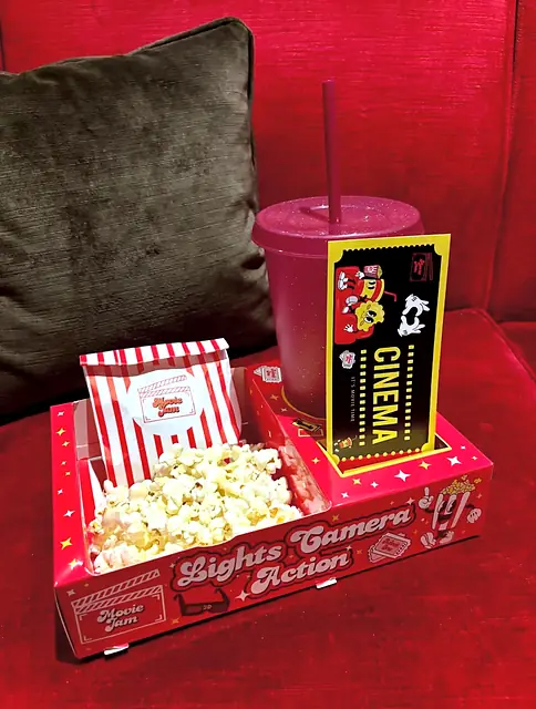 Red tray with popcorn, sweet bag and ticket cup on a red sofa