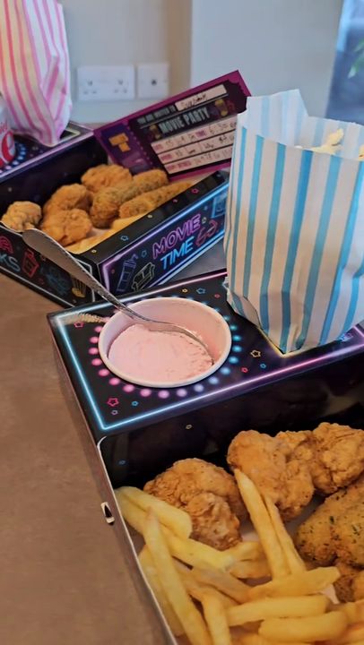 Trays loaded with chicken and chips, then a girl carries hers to a family film night