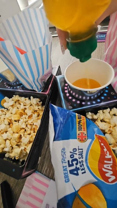 Neon trays filled with popcorn, crisps and sweet bags, then a child watching TV